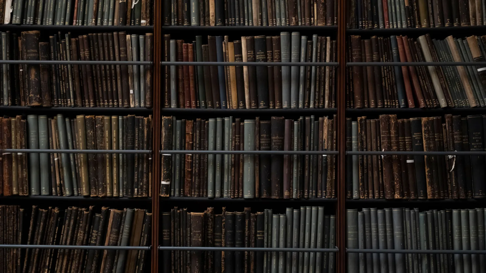 Dicht opeengepakte oude boeken op donkere bibliotheekplanken, ruggen in gedempt bruin en groen