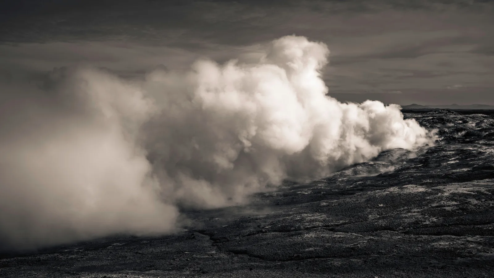 Zwart-witbeeld van een IJslandse geiser die een dikke stoomwolk uitstoot boven ruwe, donkere lavagrond