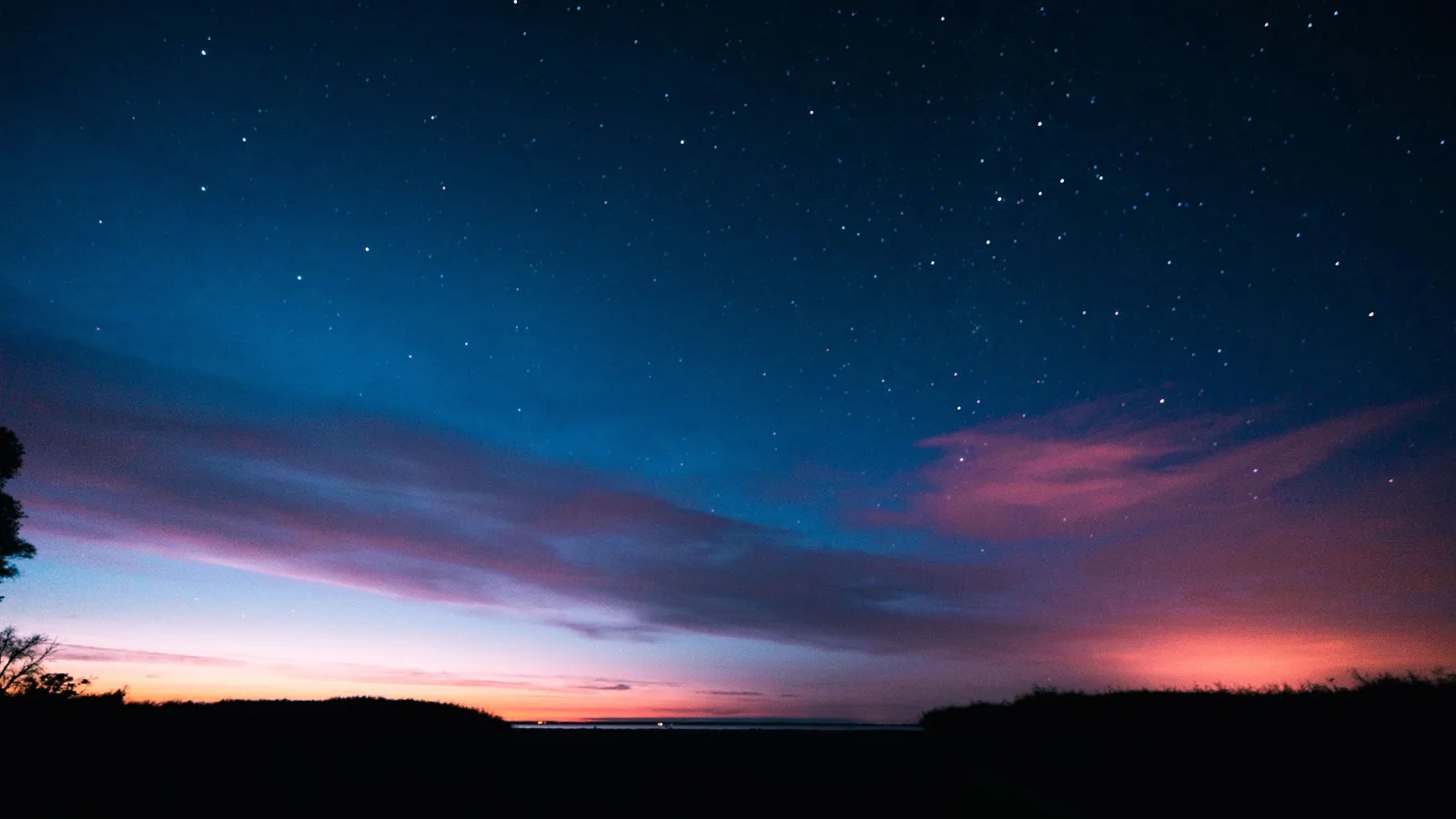 Diepblauwe schemerhemel met roze wolkenslierten boven een donkere, vlakke horizon