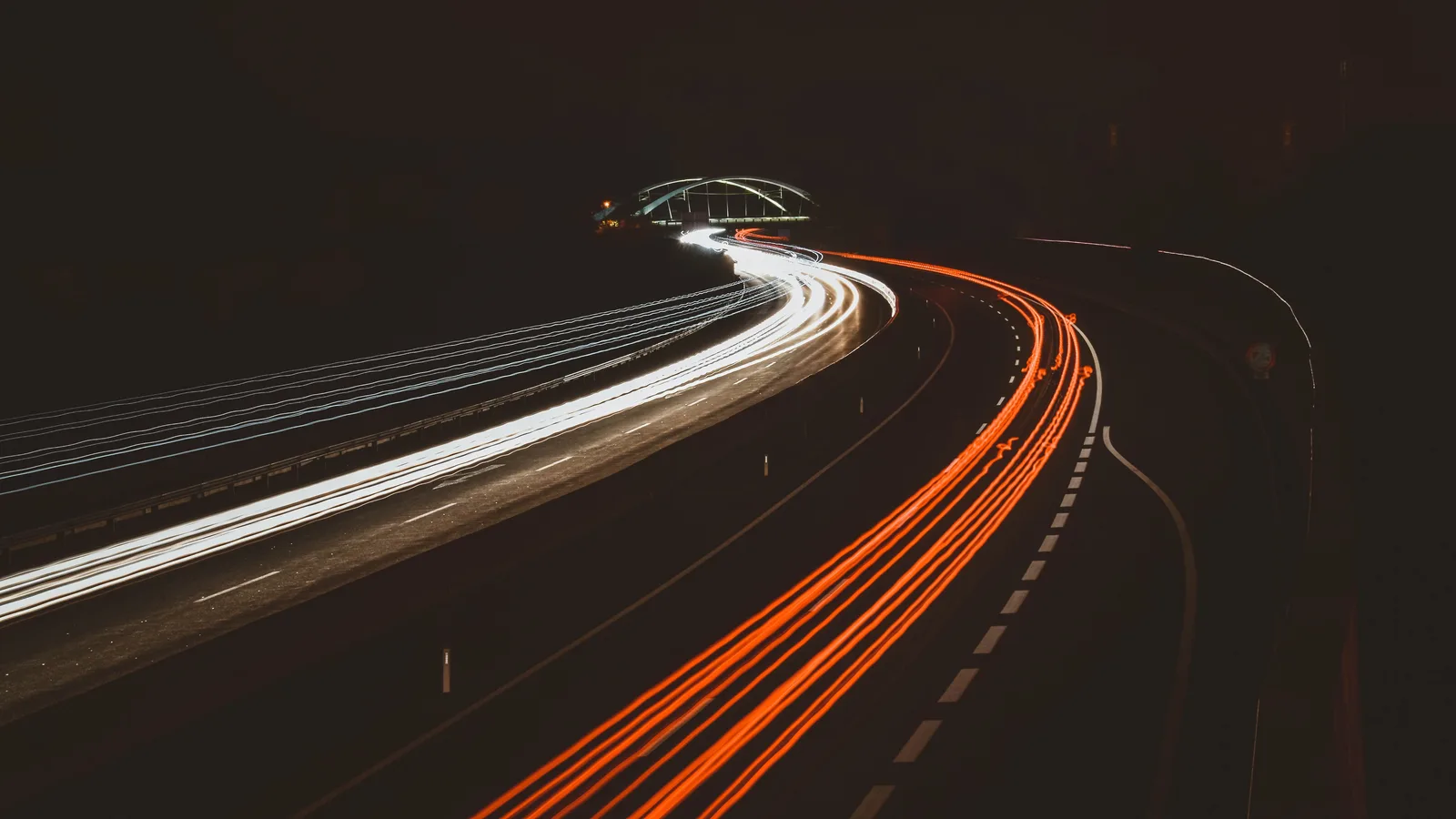 Lange sluitertijd op een snelweg bij nacht, witte en rode lichtsporen buigen door het beeld