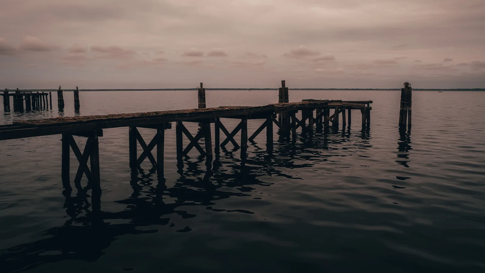 Verweerde houten pier steekt de kalme zee in onder een grijze schemerhemel