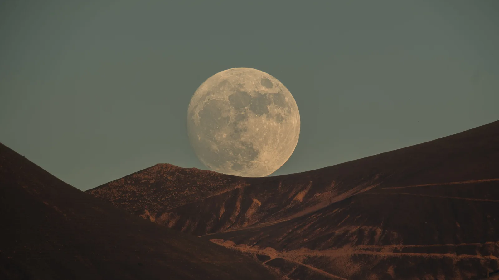 Grote volle maan komt op achter donkere bergkammen in een schemerhemel
