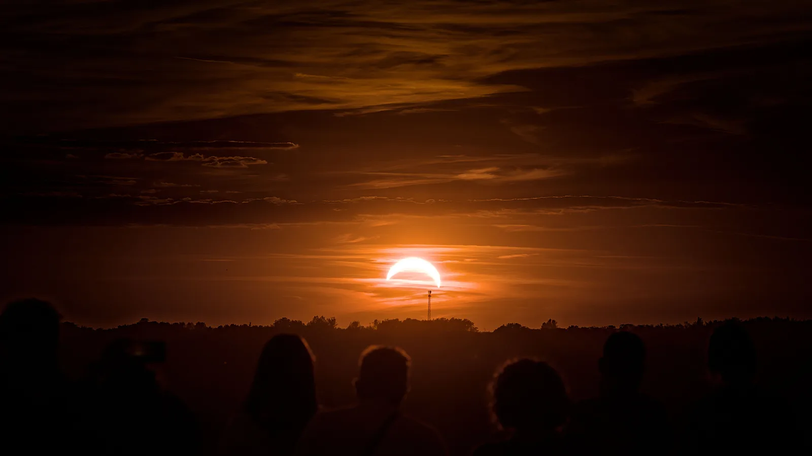 Silhouetten van toeschouwers kijken naar een gedeeltelijke zonsverduistering boven een oranje avondlucht